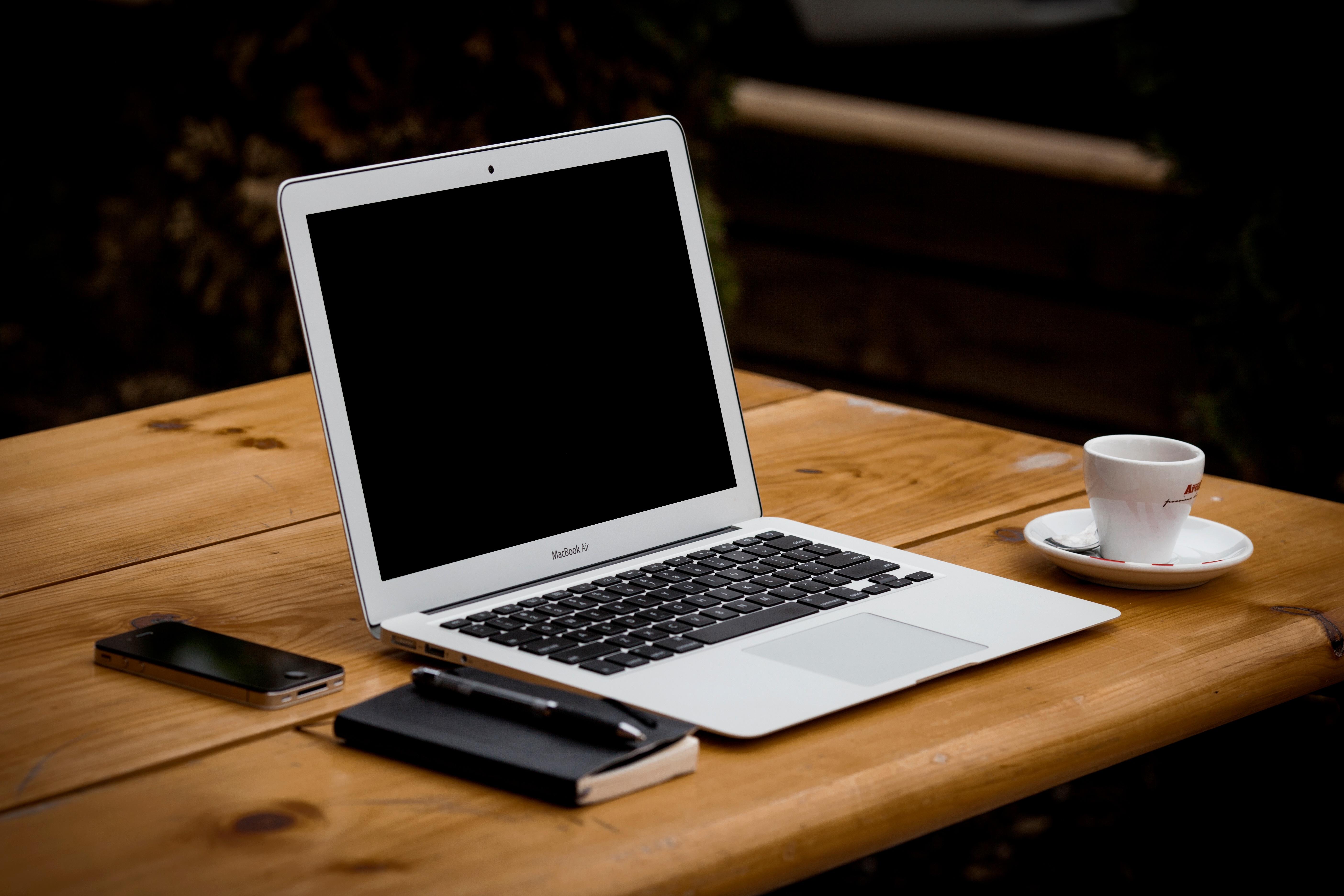 a desk setup and ready for work with a laptop computer, paper notebook, mobile phone, and a cup of espresso