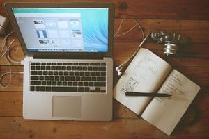 top-down photo of an open laptop computer and paper notebook on a table